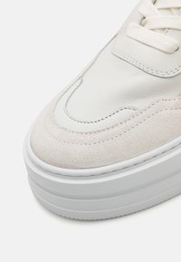 Sneaker en cuir blanc et en suède beige clair avec une épaisse semelle en caoutchouc blanc et des coutures contrastées, dotée d'un bout arrondi et d'un design à lacets.