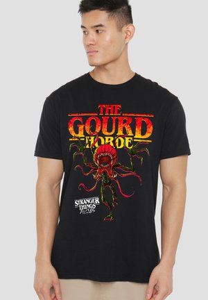 Black t-shirt with red and yellow "The Gourd Horde" text and a red monster from Stranger Things graphic on front worn by a standing man.