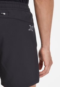 Pantalones cortos deportivos negros hechos de material ligero, con una cinturilla elástica, bolsillo lateral y un logo plateado en la parte trasera.