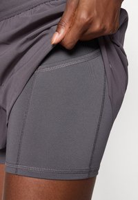 Grå treningsshorts laget av elastisk stoff, med sømløse sømmer og tettsittende passform. Teksturen er glatt og lett.