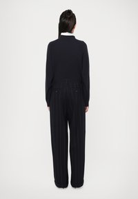 Maglione blu navy con collo alto, abbinato a pantaloni neri a righe. L'outfit presenta una vestibilità sartoriale e un design a maglia testurizzata.