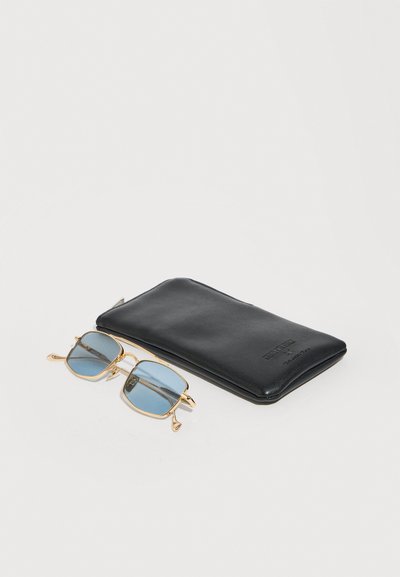Folded black leather glasses case next to gold-framed eyeglasses with blue-tinted lenses on a white background.
