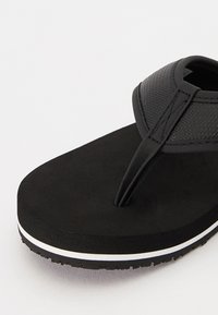 Sorte flip-flops med teksturerte stropper og polstret såle. Har en hvit dekorstripe langs sålen. Gummisåle for godt grep.
