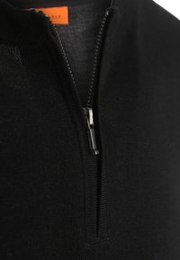 Zwarte gebreide trui met een kwart-rits kraag, soepele textuur en zilveren rits hardware. Inclusief een oranje label aan de binnenkant.
