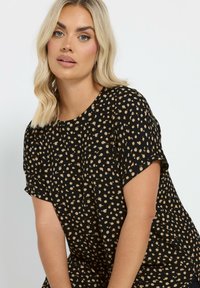 Maglietta nera a maniche corte, con un motivo di macchie beige. Il tessuto è leggero, con una vestibilità comoda e scollo rotondo.