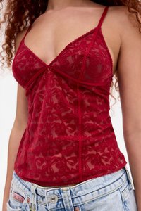 Camisetta in pizzo rosso con ricami floreali, coppe triangolari e spalline regolabili, con orlo a onda e texture morbida. Indossata sopra dei pantaloni corti in denim.
