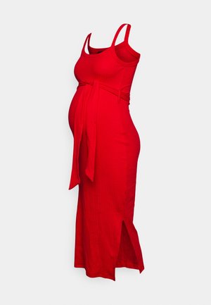 Red ribbed maternity dress with spaghetti straps, side tie belt, and thigh-high slit. Smooth texture and form-fitting silhouette.