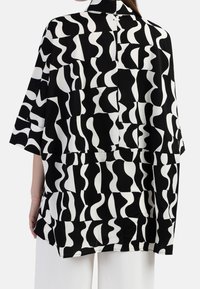 Sorte og hvide mønstrede kimono med en løs pasform, der har abstrakte former og en krave-design. Glat tekstur og korte ærmer.
