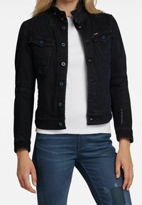 Musta farkkutakki, jossa on istuva malli, siniset napit, kaksi rintataskua ja korkea kaulus. Päällä valkoinen paita.