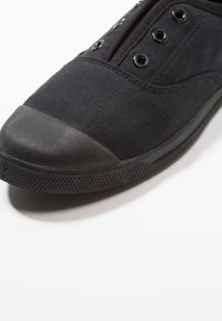 Svart canvas sneakers med en rund, gummitåhuvud, metallöljett och texturerad sula. Enkel design med en slät, matt yta.