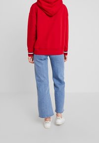 Felpa con cappuccio rossa, con polsini a righe bianche e blu navy, abbinata a jeans larghi blu chiaro e sneakers bianche con dettaglio logo.