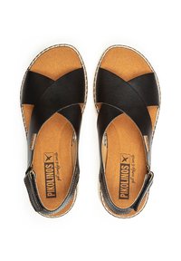 Sandalias de cuero negro con diseño de tiras cruzadas, plantilla color marrón claro y costuras decorativas. Cuenta con una correa en el tobillo con herrajes ajustables.