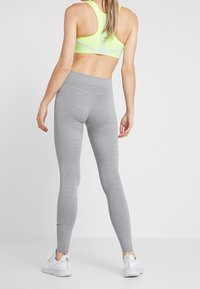 Leggings grigi con design senza cuciture e vita alta, abbinati a un reggiseno sportivo giallo neon con righe e stile racerback.