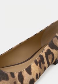 Παντόφλα με λεοπάρ σχέδιο, στρογγυλεμένη μύτη και μπεζ εσωτερική επένδυση σε λευκό φόντο.