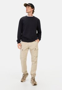 Dunkelgrauer Rundhalsausschnitt-Pullover, bequeme beigen Cargo-Hosen mit Taschen und beigen Sneakers. Glatte Textur, lässige Passform und funktionale Design-Details.
