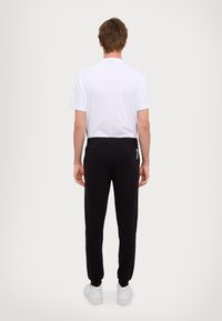 Zwarte sweatpants met een elastische tailleband, gecombineerd met een effen wit T-shirt. Heeft een minimalistisch ontwerp en witte branding op de broek.