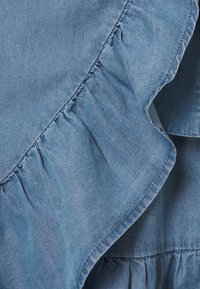Denim fabric with a light blue color, featuring a ruffled edge and gathered texture. Stitched detailing along the seams.