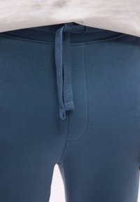 Κοντινό πλάνο μπλε παντελονιών φόρμας με ελαστική μέση και κορδόνι και ένα λευκό πουκάμισο που είναι μπα tucked πάνω από τη μέση.