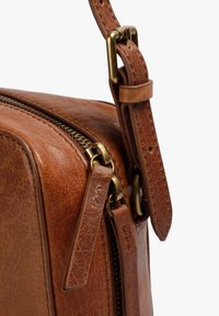 Brown leather bag with a textured surface, featuring brass hardware, a zipper closure, and an adjustable strap.