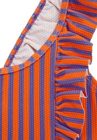 Ribota frotinės medžiagos oranžinė ir violetinė juostelėmis, su raukšlėta detale palei kraštą. Minkšta tekstūra ir atsipalaidavęs siluetas.