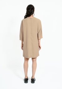 Rochie scurtă bej cu o siluetă simplă, mâneci pana la cot și fermoar la gâtul din spate. Textură netedă și design minimalist.