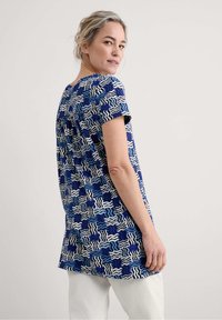 Mėlynas raštuotas marškinėliai su abstrakčiais bangų dizainais, įvairių mėlynų ir baltų atspalvių, trumpomis rankovėmis ir laisvu siluetu.