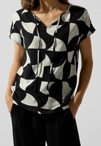 Haut en noir et blanc à motif, avec un décolleté en V, des manches courtes et des détails à cordon. Le tissu a une texture lisse et une coupe décontractée.