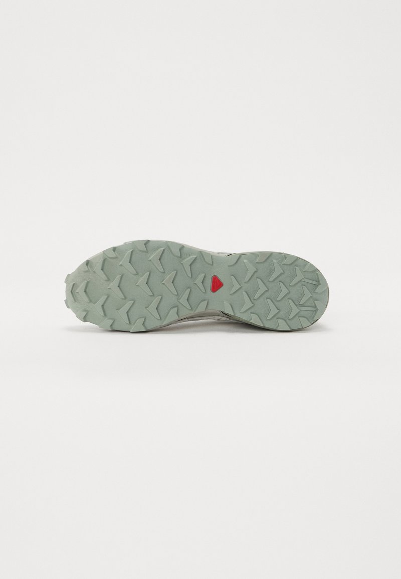 Suela de zapato de trail running con una superficie de goma texturizada. Los colores presentan tonos de verde menta con un acento rojo. Diseñada para tracción.