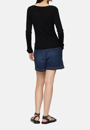 Haut à manches longues noir côtelé, short en denim bleu avec ourlet roulé et sandales plates noires. Détails de couture visibles et coupe décontractée.