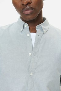 Camisa azul celeste de botones con cuello con solapas, botones blancos y un ajuste cómodo. La tela presenta una textura suave y un brillo sutil.