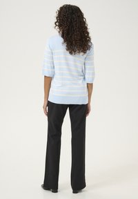 Heled sinine lühikeste varrukatega kampsun valgete triipudega, pehme kudumise tekstuuriga. Kombineeritud mustade pükstega, mis näitavad sirget jala disaini ja minimaalset detailide kasutamist.