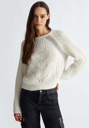 Maglione lavorato a maglia di colore crema con un motivo testurizzato, colletto e polsini a coste. Abbinato a pantaloni cargo scuri con dettagli in zip.