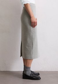 Šedá pletená sukně s rovný střih, se stranovým rozparkem a hladkým povrchem, spárovaná s tmavými loafers a šedými ponožkami.