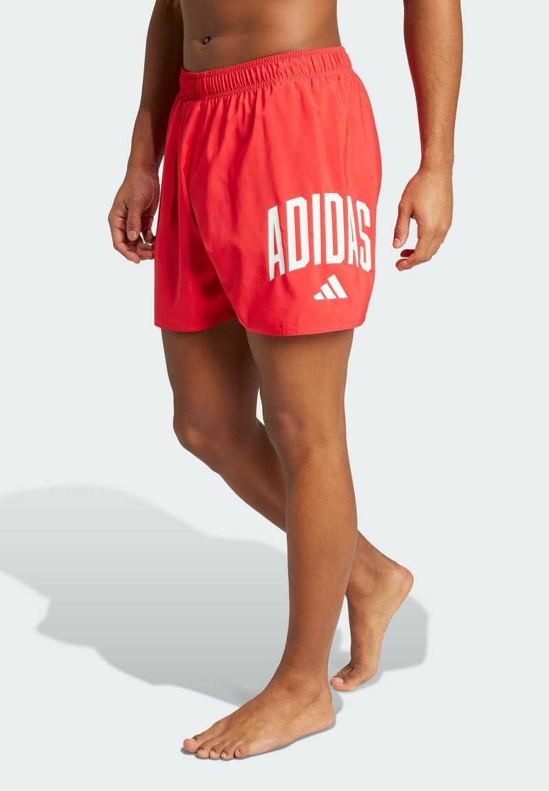 Červené plavky vyrobené z ľahkej tkaniny s elastickým pásom. Obsahujú biele logo "ADIDAS" a ikonický trojuholníkový akcent po strane.