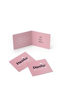 Rozā salocīta kartīte ar melnu tekstu "Danke" un baltām akcentiem. Iekšpusē ir vieta roku rakstītai ziņai uz maigi rozā fona.