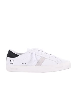 Sneaker bianca con tomaia in pelle liscia e accentuazione nera sul tallone, caratterizzata da una striscia argentata e lacci bianchi. Suola in gomma spessa.