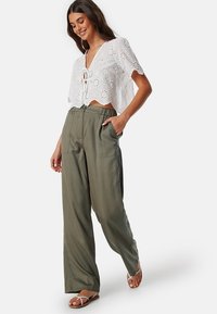 Witte, geborduurde crop top met een strik aan de voorkant; gecombineerd met hoge, olijfgroene wijde broek en sandalen met bandjes.