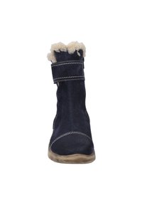 Mørkeblå ruskindsankelstøvle med en blød cremefarvet pelsforing øverst, en velcrorem og kontrasterende hvid syning langs kanterne.