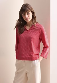 Rot gestreifte Bluse mit V-Ausschnitt und dreiviertel Ärmel, ausgestattet mit einer weichen Textur und einer lässigen Passform, kombiniert mit hellen Hosen.