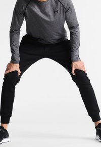Grau langärmliges Sportshirt und schwarze taillierte Jogginghose, beide mit glatter Textur. Das Outfit ist für Komfort und Beweglichkeit konzipiert.