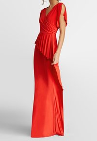 Robe rouge jusqu'au sol en tissu lisse, présentant un buste drapé, un peplum volanté et des manches flottantes.