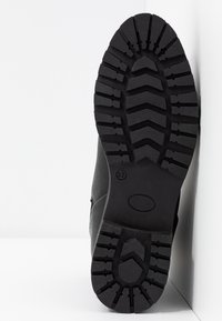 Svart boot sole med ett robust mönster för grepp, tillverkat av hållbar gummi med strukturerade detaljer och en stadig konstruktion.