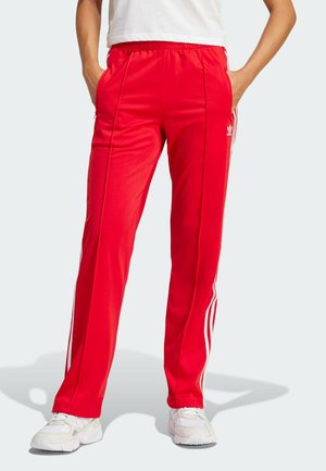 Rote Sporthosen aus glattem Stoff, mit weißen Seitenstreifen und einem elastischen Bund. Enthält seitliche Taschen für Funktionalität.