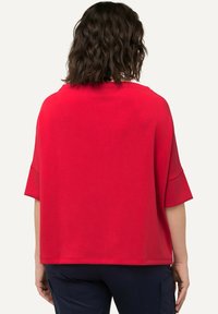 Haut rouge à manches courtes avec une coupe décontractée et un col rond. Tissu lisse avec une texture subtile, tombant jusqu'à la taille.