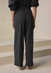 Čierne nohavice s vysokým pásom, širokými nohavicami a hladkou textúrou. Majú dve zadné vrecká a jemnú záhyb, kombinované s ľahkými teniskami.