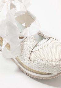 Vita sneakers med sprucken textur, nätpaneler och tygsnören. Har en tjock sula med en gulddetalj och en platt, bred form.