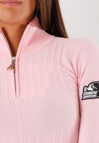 Pullover rosa chiaro a tre quarti con zip, caratterizzato da una texture a coste, dotato di una patch con logo e zip argentata. Tessuto morbido, design aderente.