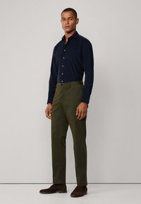 Marineblauwe overhemden met lange mouwen, gecombineerd met olijfgroene slim-fit broek en bruine suède schoenen. Eenvoudig ontwerp, op maat gemaakt pasvorm en subtiele texturen.