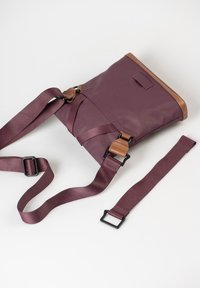 Lila Tasche aus robustem Material, mit einem braunen Lederoberteil, verstellbaren Trägern und Metallbeschlägen für einen sicheren Verschluss.