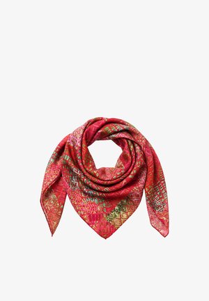 Kobieta z falującymi brązowymi włosami, ubrana w czerwony apaszka we wzory, spogląda przez ramię z neutralnym wyrazem twarzy na jednolitym tle.